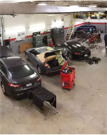 Multiple vehicles undergoing collision repair inside Modern Carriage Werks auto body shop, with technicians working on insurance claim repairs